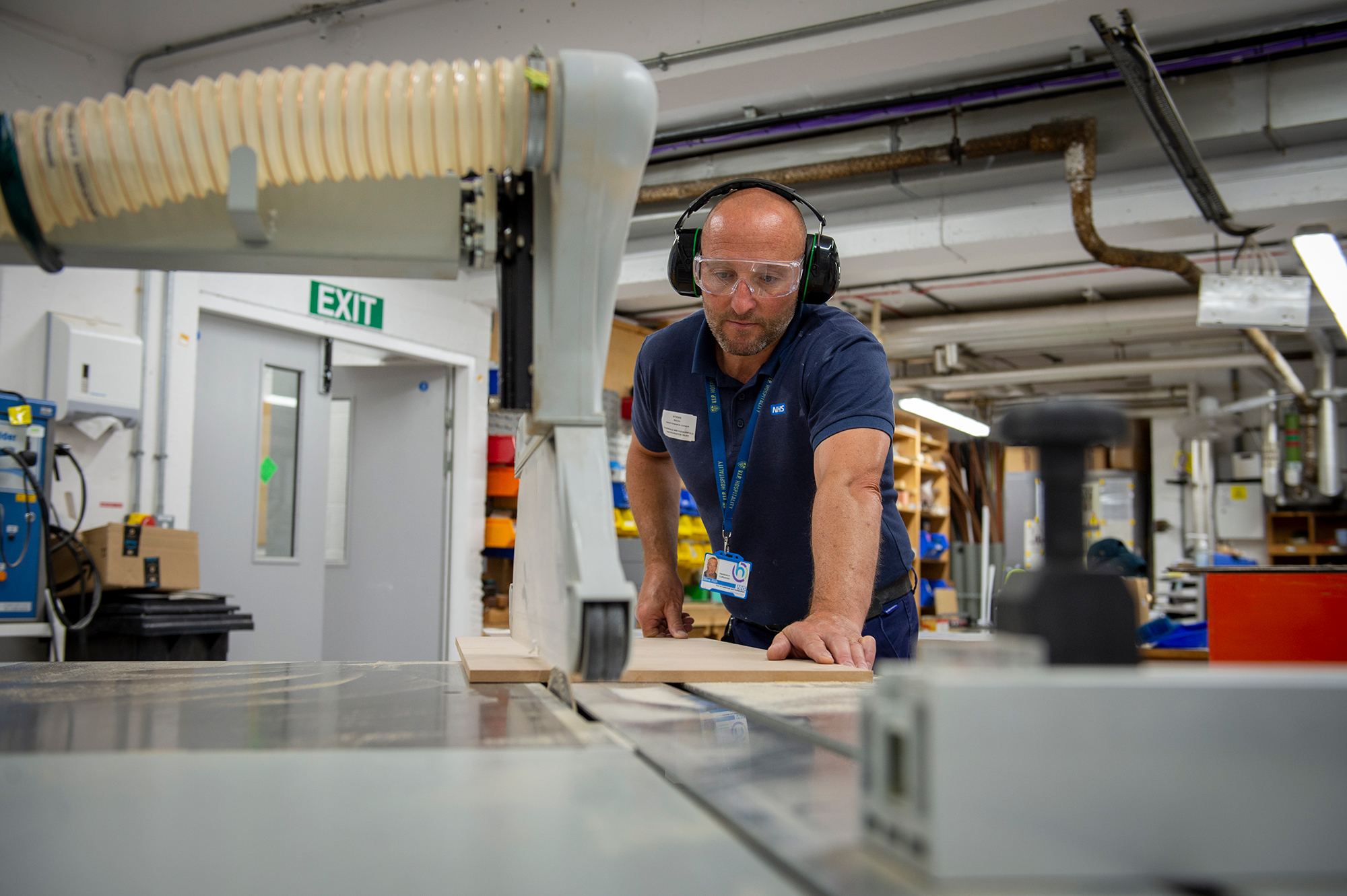 Male employee cutting wood with a machine wearing protective gear.