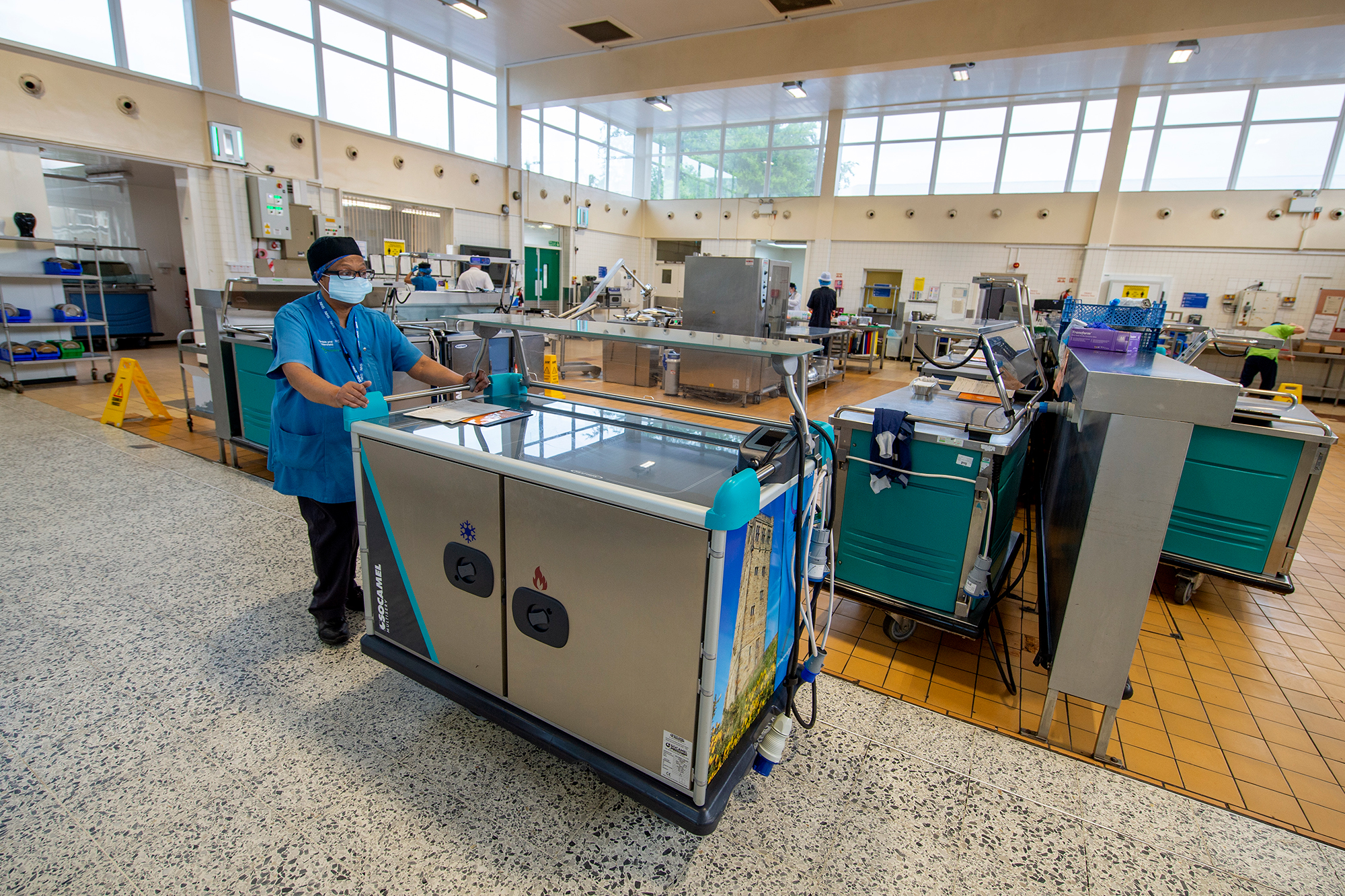 Female employee pushing large food container in the kitchen.