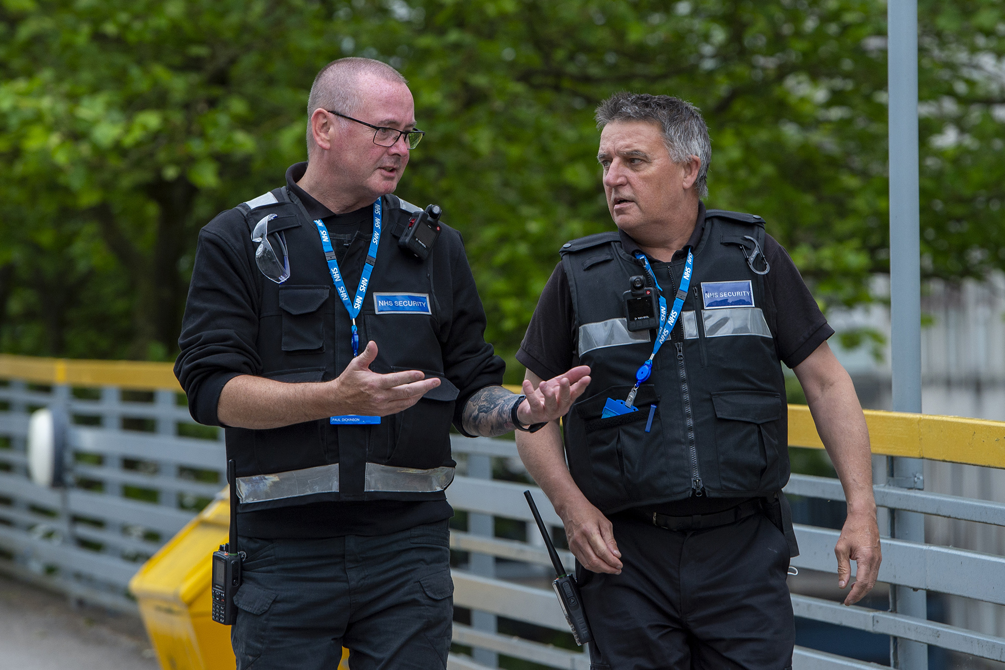 Two male security guards walking at a hospital site talking to each other.