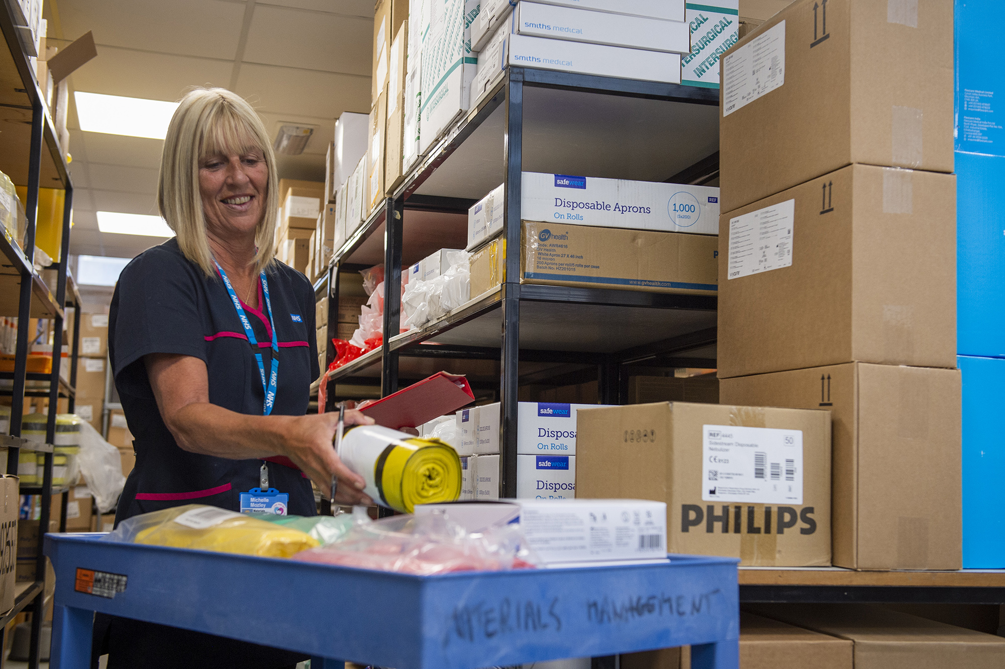 Female staff member picking up equipment from a stores warehouse.