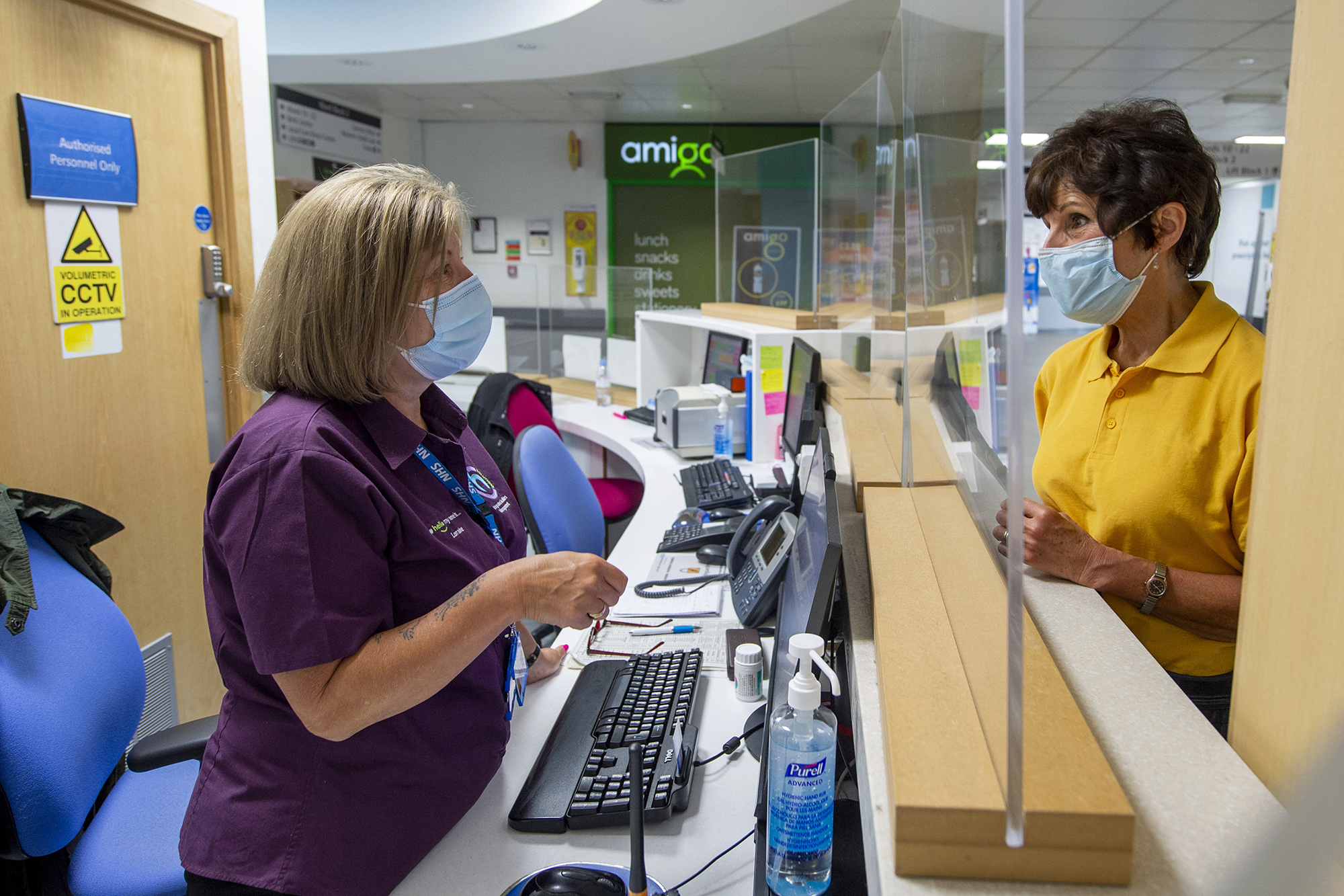 Patient at the hospital taking to a member of staff behind a reception desk.